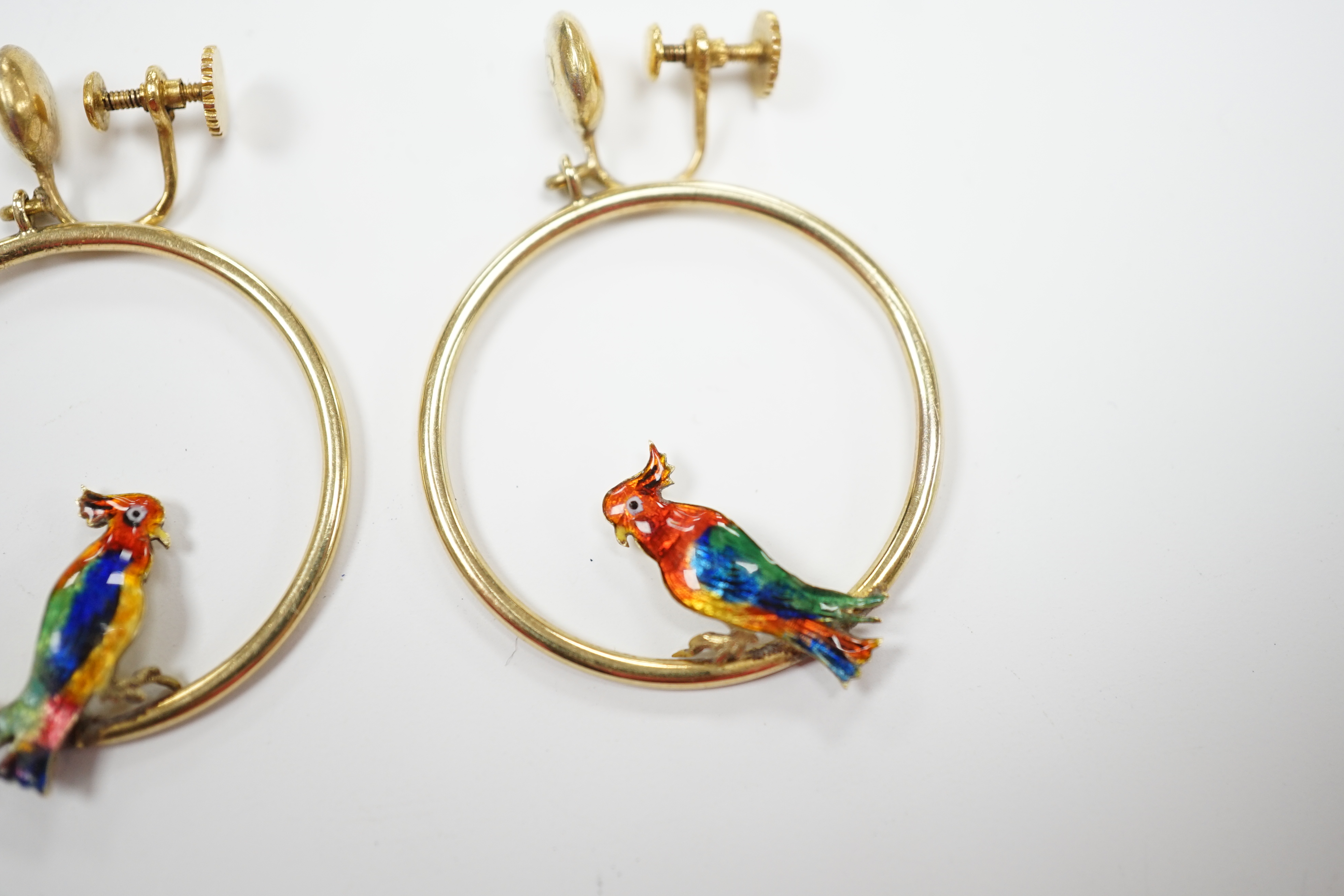 A pair of early 20th century 15ct loop ear clips, with a polychrome enamelled parrot perched upon each, diameter 30mm, gross weight 7.3 grams.